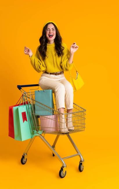 White woman laughing while sitting in shopping cart isolated over yellow background