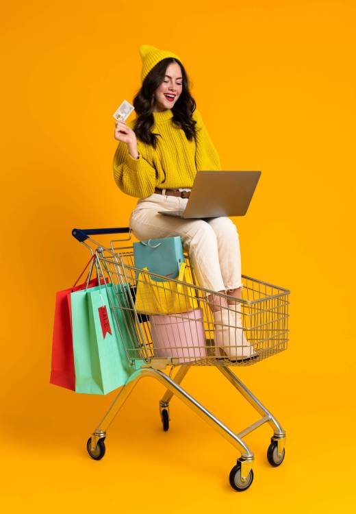 White woman using laptop while sitting in shopping cart isolated over yellow background