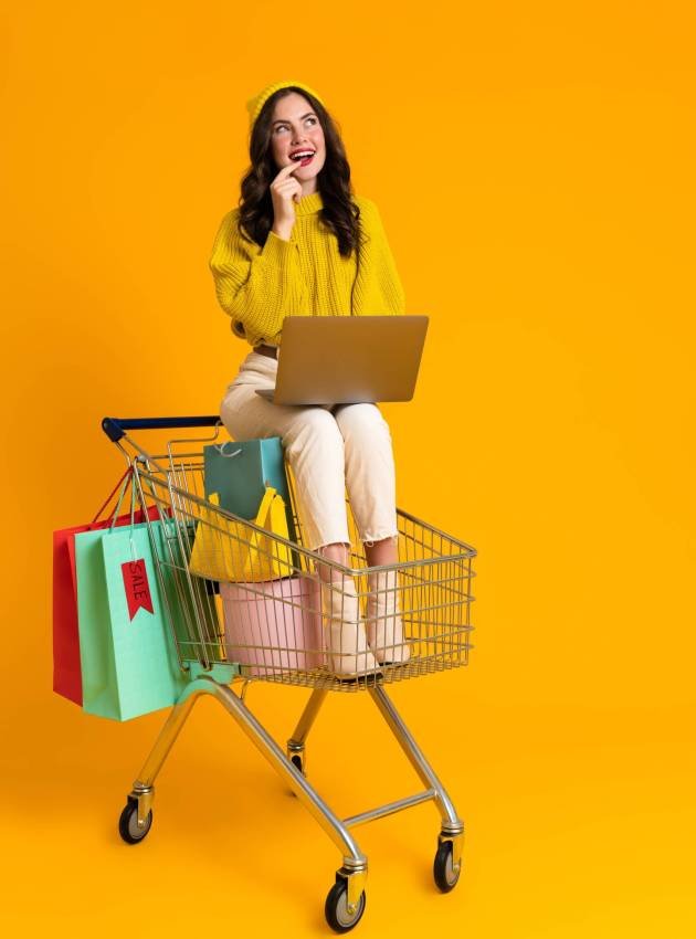 White woman using laptop while sitting in shopping cart isolated over yellow background